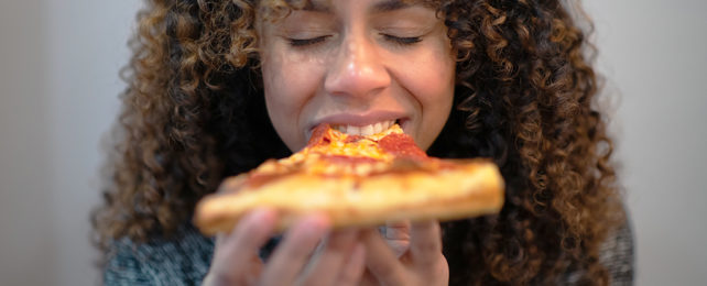 Woman eating a slice of pizza with her eyes closed