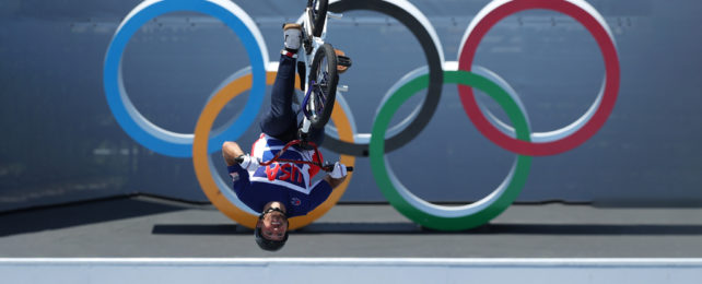 BMX rider upside down on bike in mid air in front of Olympic logo