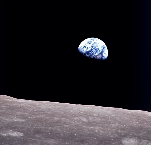 Distant image of Earth against a black background, with the moon's surface in the foreground