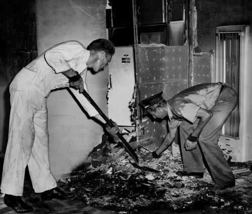 Black and white image of firemen investigating burnt disintegrated remains