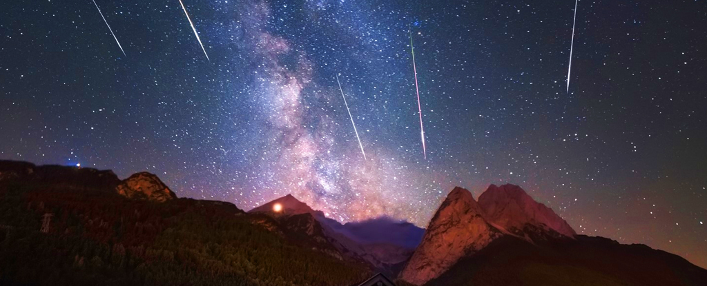 Meteor shower in front of Milky Way falling over jagged hills