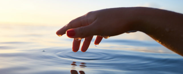 A wet hand hovers over ocean water.