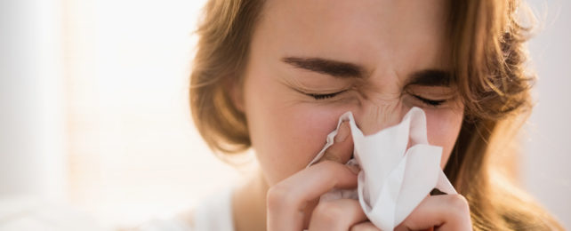 A woman blows her nose into a facial tissue.