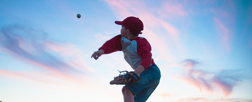 Kind wirft einen Baseball gegen einen blauen Himmel
