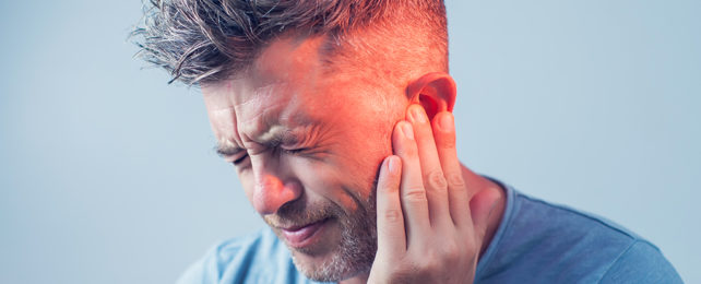 man holding his ear with a pained look on his face