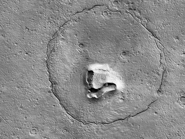 Scratchy circle on cratered Mars surface with what look like two eyes and a snout