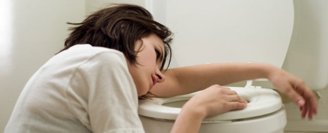 A sick woman leans against a toilet.