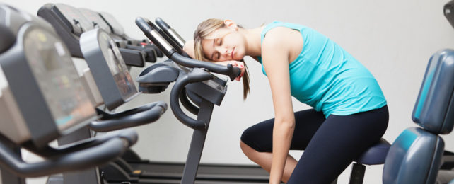 A woman sleeps on an exercise machine.