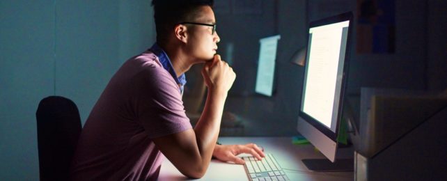 Young Man Sits At Computer In Darkness