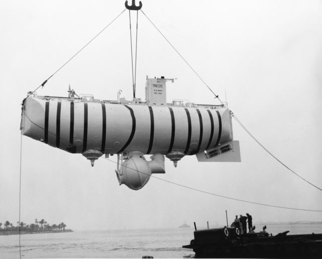 Black and white image of old submarine hoisted over the water