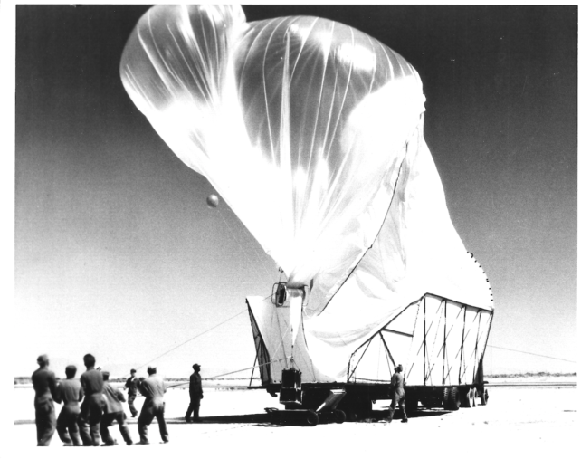 Black and white image of people holding down inflating big white balloon