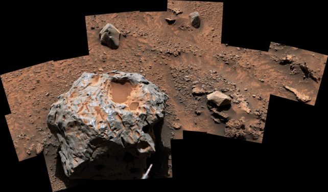 A big rock covered with red dust on red dirt surrounded by smaller rocks