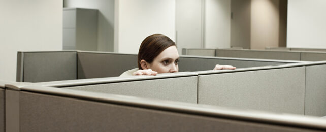 A woman peeks creepily over a cubicle wall.