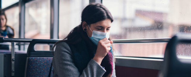A woman wearing a mask coughs while riding on a bus.