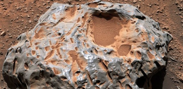 Details of a silvery rock covered with red dust and lots of grooves