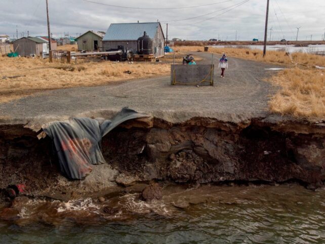 Road crumbling into meltwater with houses nearbye.