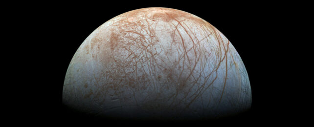 Icy moon's surface streaked with reddish dirt, floating in space.