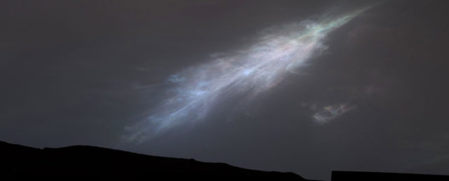 Wispy feather shaped clouds against dark star studded sky, over dark slopes with iridescent hints of blue, green and pink.