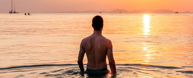 Man standing in ocean water with the sun near the horizon