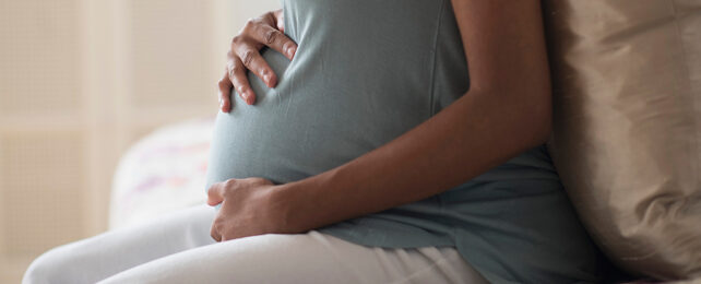 black mother in a blue shirt, image cropped to focus on her pregnant belly