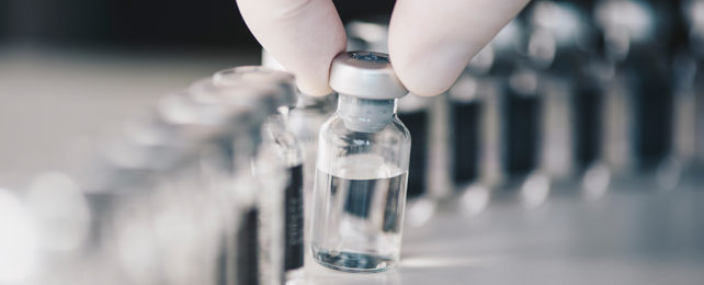 vial of clear liquid being held by gloved fingers