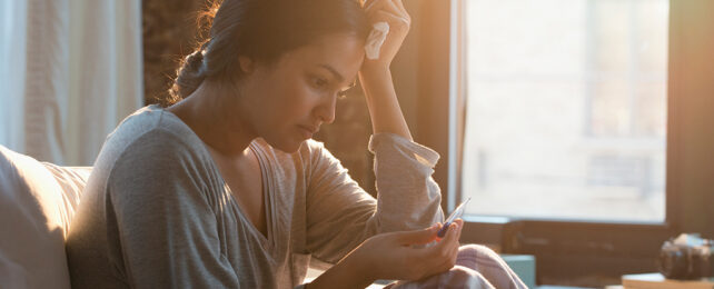 Hispanic woman with a disappointed expression looking at a pregnancy test