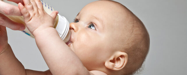 Baby reaching up to hold a bottle