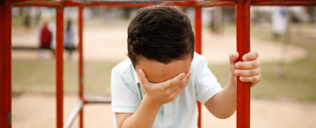 A child sits on a jungle gym with his face in his palm.