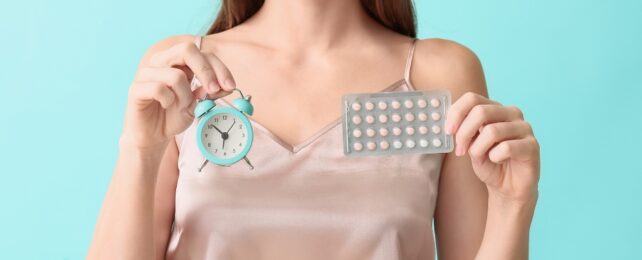 A photo of a person's torso showing their hands holding a packet of pills and a clock.