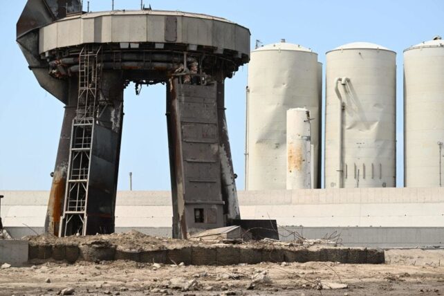 Damaged fuel tanks behind debris littered launchpad