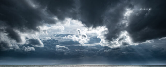 Dark clouds gather over a body of water.