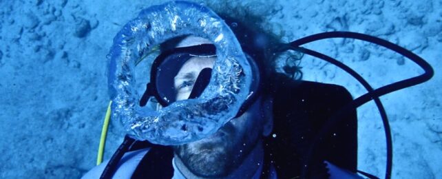 A human in diving gear laying on the ocean floor underwater.