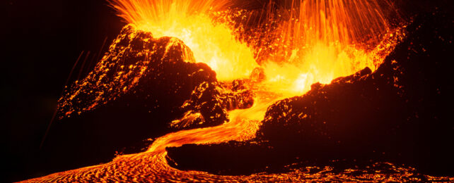 Lava exploding from volcano top and pouring into a glowing river