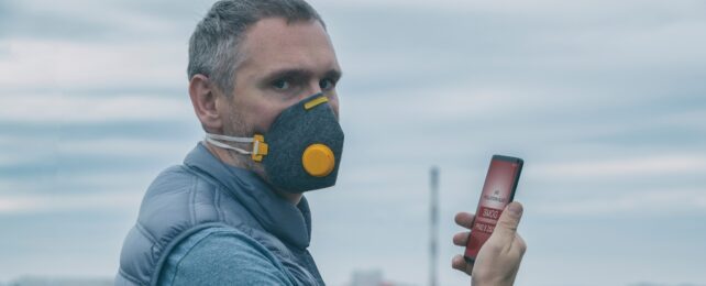 A man wearing a real anti-smog face mask and checking current air pollution with smart phone app.