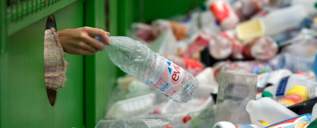 Outstretched places plastic bottle into recycling bin.