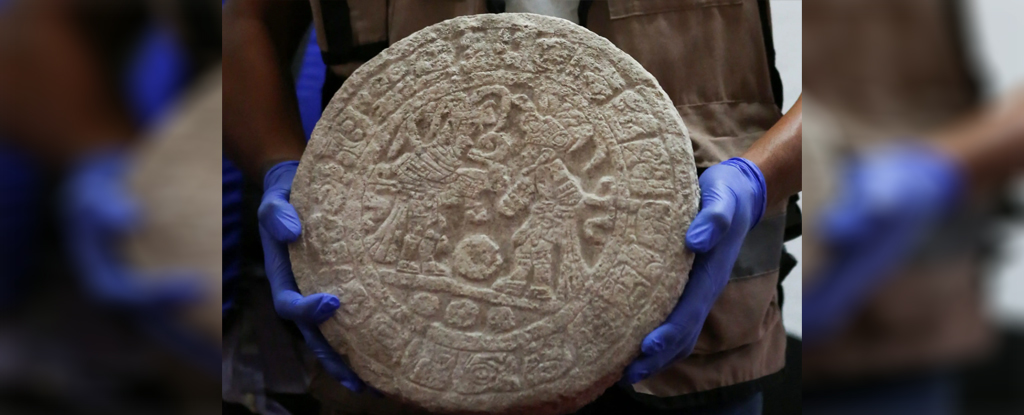 A round stone tablet with ancient Maya carvings on it.