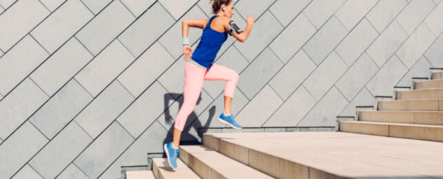 Woman with curly hair wearing pink tights and blue top running up set of stairs.