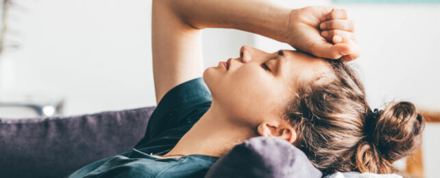 Young woman with brown hair in ponytail lying on couch with fist on forehead.