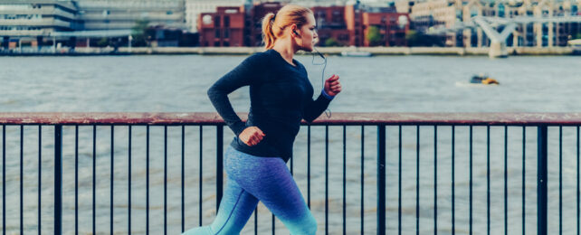 A woman runs along an urban river bank.