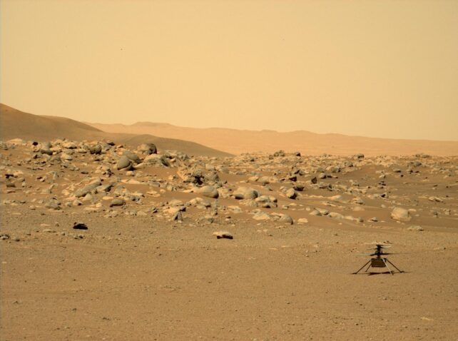 An image of a rock field on Mars also showing the Ingenuity Mars Helicopter in the bottom right corner.