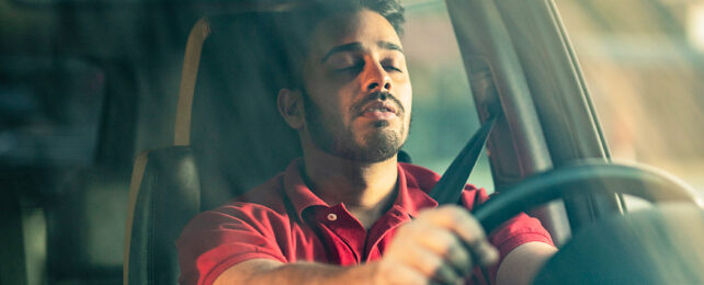 Man behind steering wheel with his eyes half closed