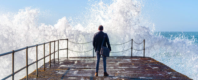 Man standing on a jetty watching a wave break over the end