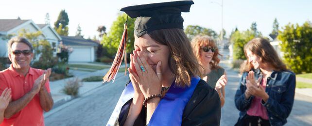 woman in black gown and mortar crying tears of joy at graduation, surrounded by family