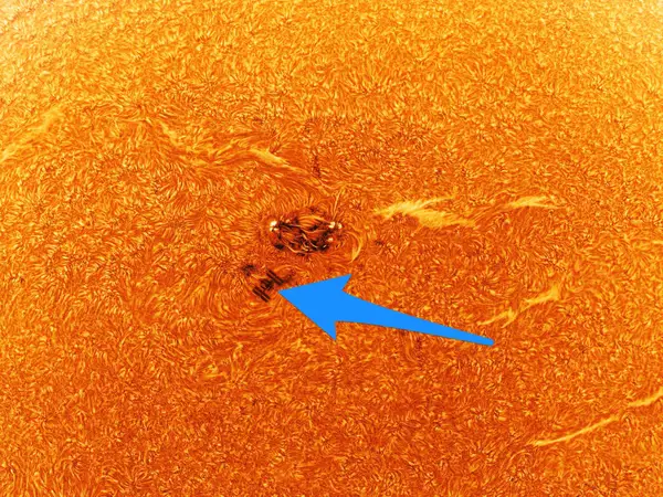 An even closer image of a small section of the sun, showing the darker area (sunspot) and the International Space Station (indicated by a blue arrow).