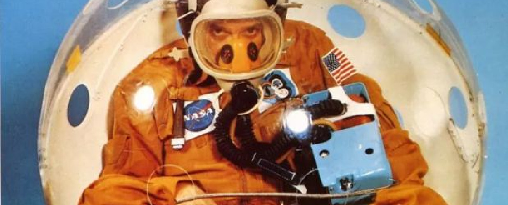 Astronaut in orange suit sitting inside clear orb, a demonstration of NASA's personal rescue ball.