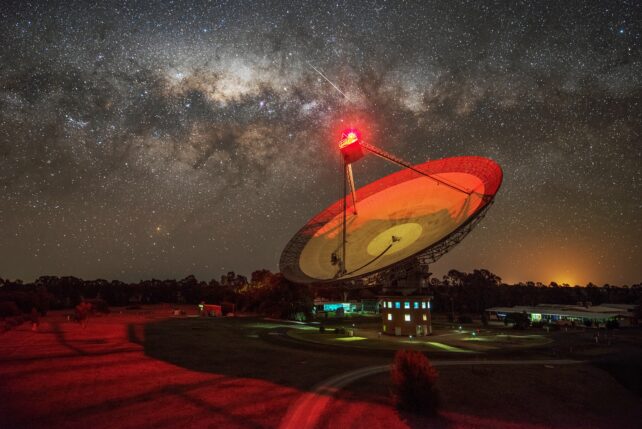Een afbeelding van de CSIRO Parkes radiotelescoop met een sterrenhemel op de achtergrond. 