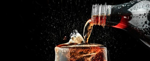 A bottle pouring cola into a glass on a back background