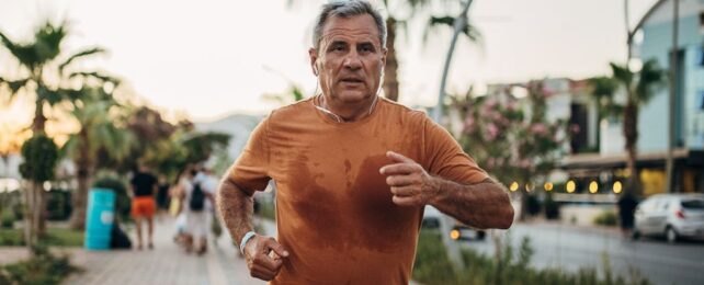 Older man running on street wearing orange t-shirt.