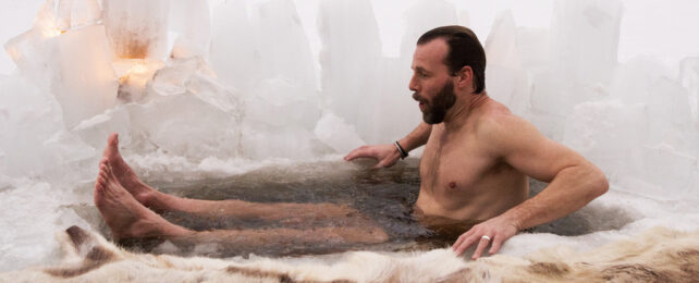 Man lowering himself into icy hole in frozen lake