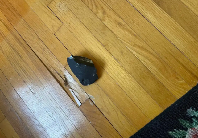 Zoomed out image of a dark rock on floorboards and a dent in the floorboards next to it